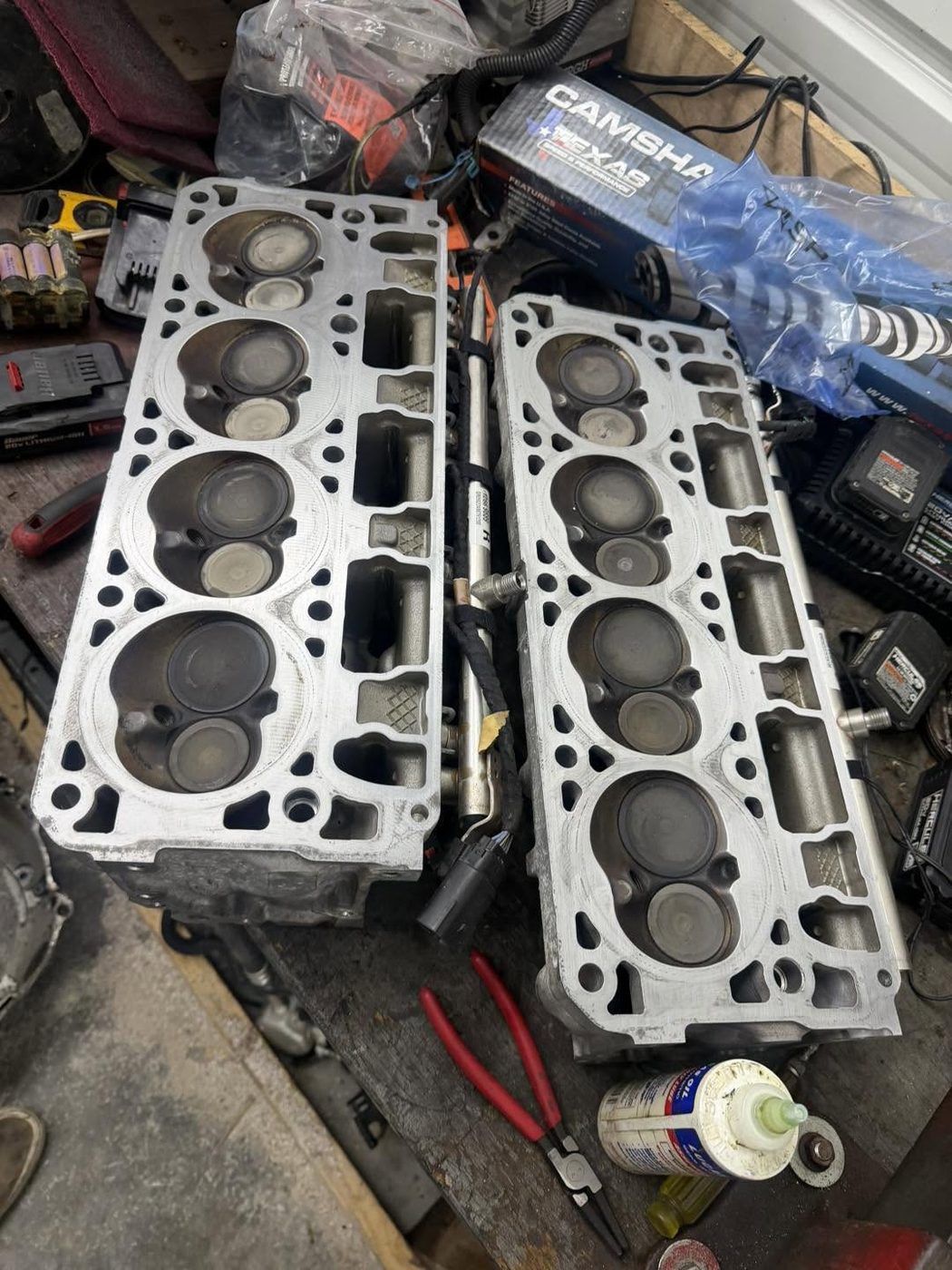 A pair of cylinder heads on the bench beside a camshaft